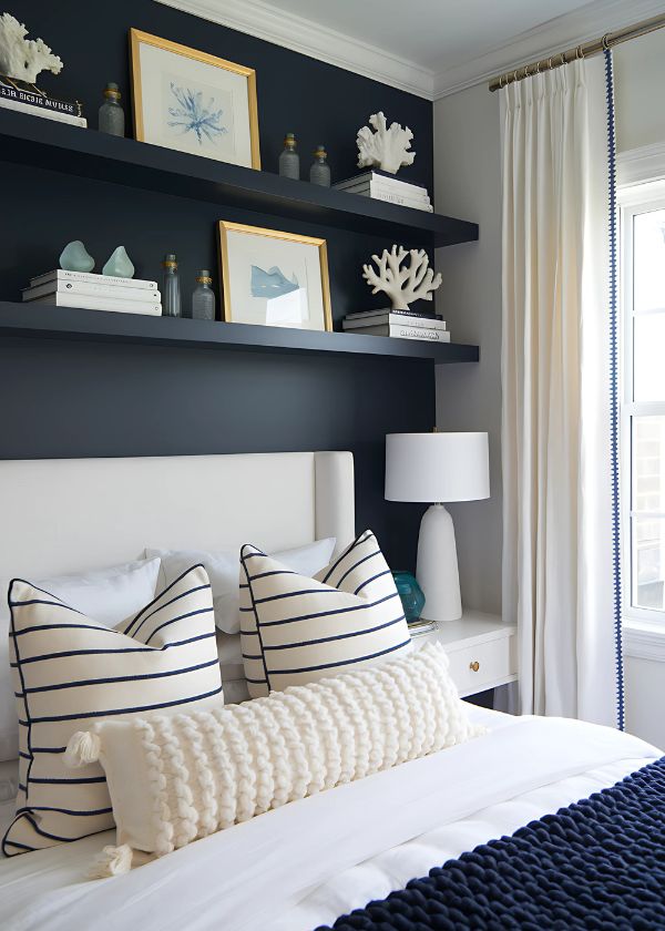 Floating shelves with coastal decor above bed in a navy and white room.