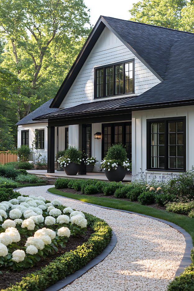 Elegant front yard with white flowers, black planters, and a crushed stone path.