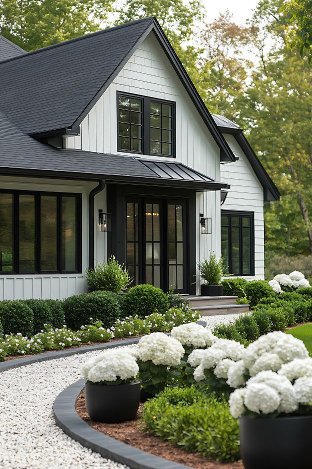 Black-and-white home with manicured greenery and white hydrangeas along a curved path.