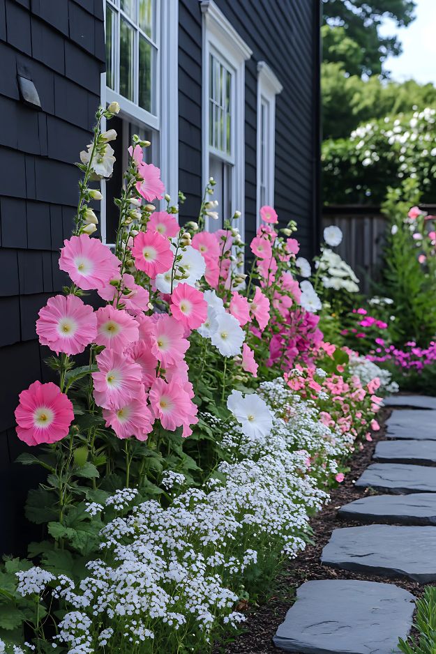 Pink and white flowers layered along dark house siding