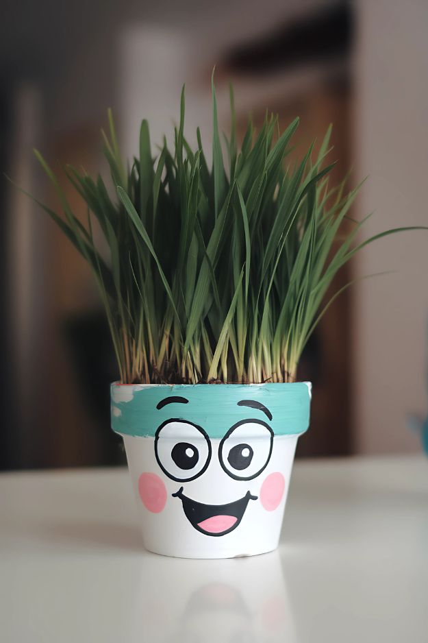 A pot with a cartoon face painted on the front and tall green grass growing from the top like hair.