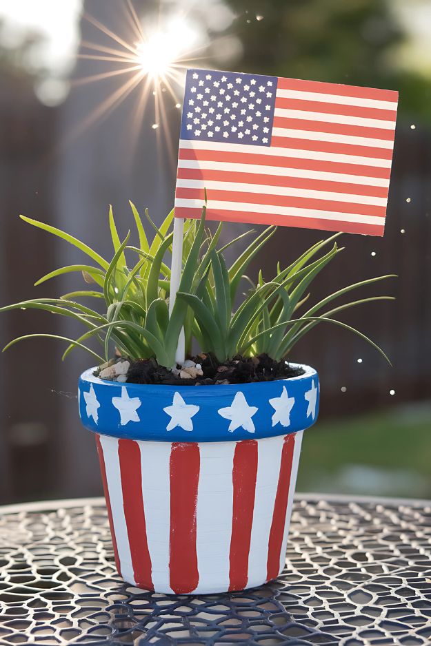 A pot painted with red stripes, a blue rim with white stars, and an American flag sticking out from the plant.
