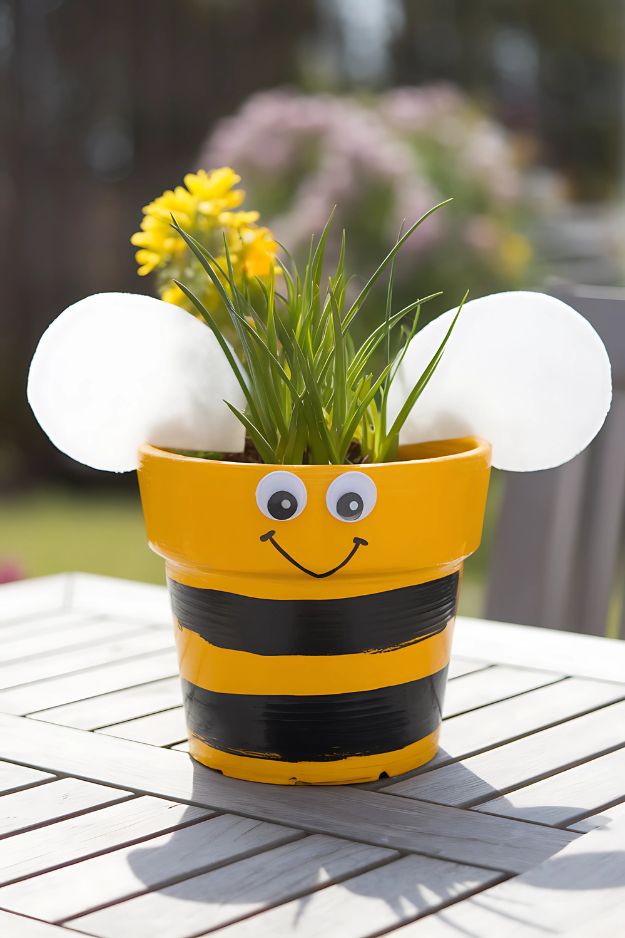 A yellow flower pot painted with black stripes and googly eyes, plus two white wings on each side.