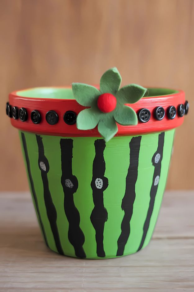 A green and red flower pot painted like a watermelon with black stripe seeds and button accents.