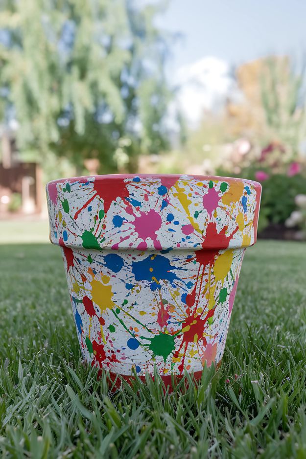 A white flower pot covered in colorful splatter paint designs, sitting on green grass