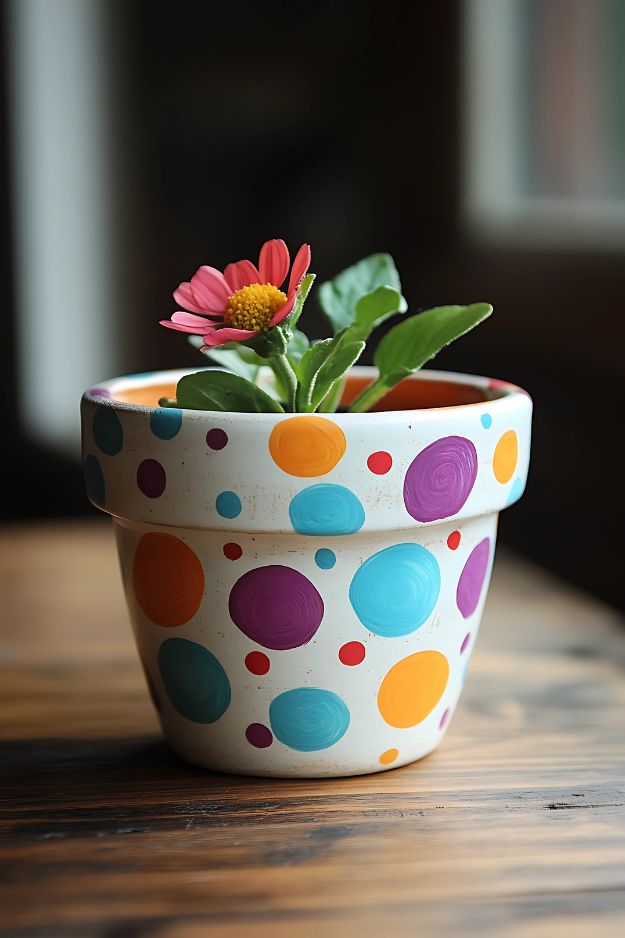 A cream-colored pot decorated with large and small colorful polka dots, holding a single flower.