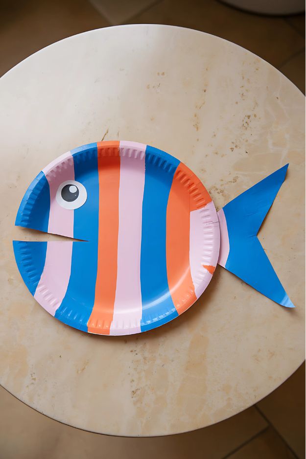 Summer crafts for kids of Striped paper plate fish with pink, blue, and orange paint and a triangle tail.