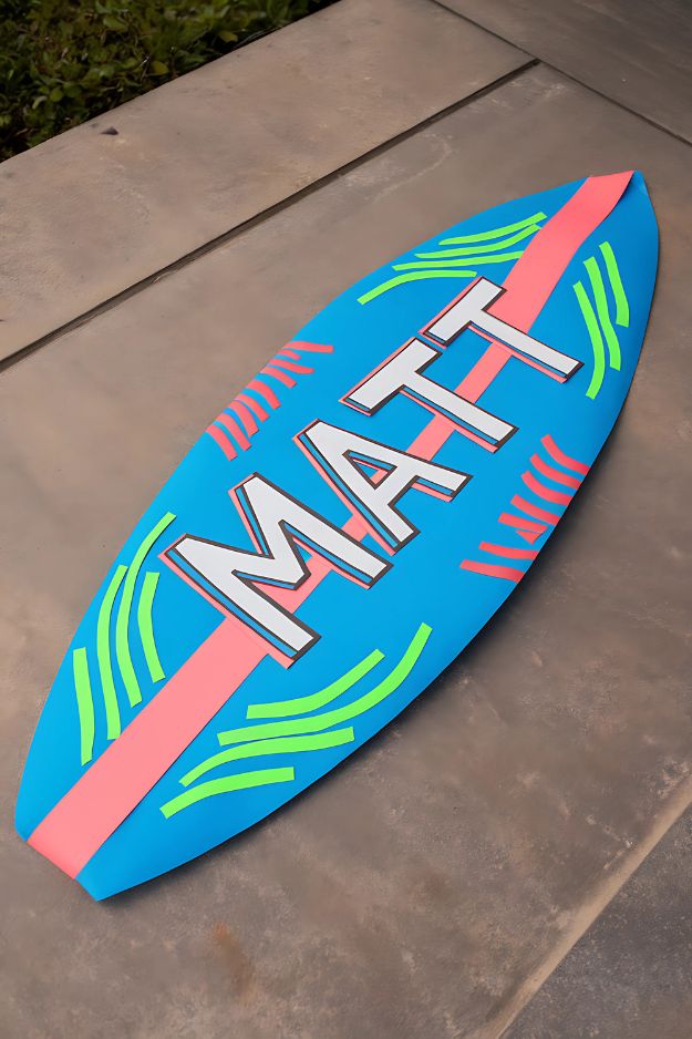 Bright blue paper surfboard with neon decorations and the name “Matt” in bold letters.