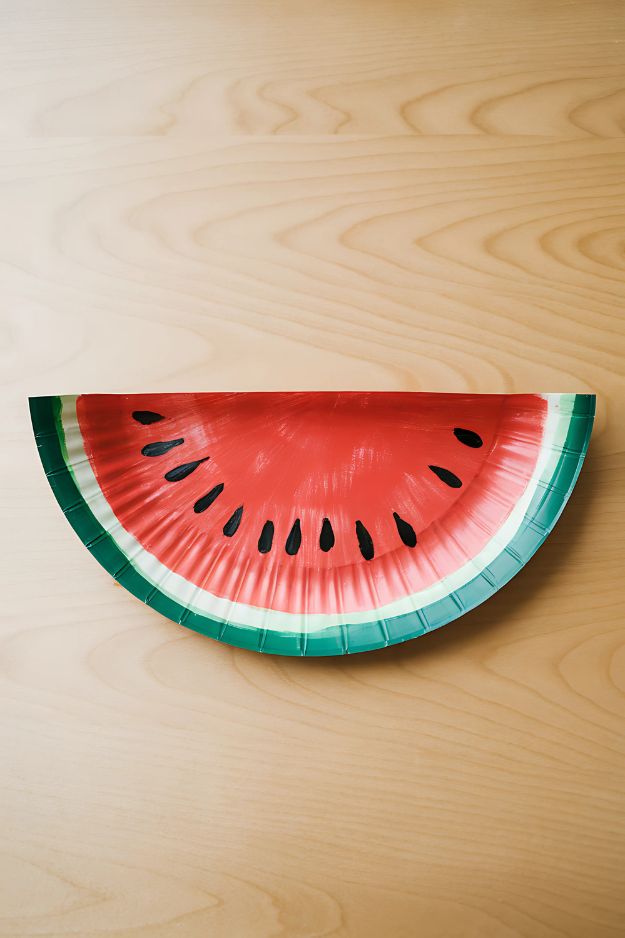 Half-circle paper plate painted like a watermelon slice with red center, green rind, and black seeds.