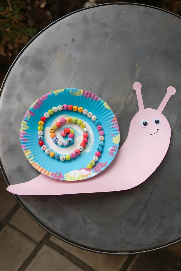 Colorful snail craft with a painted paper plate shell decorated with beads and a pink paper body.