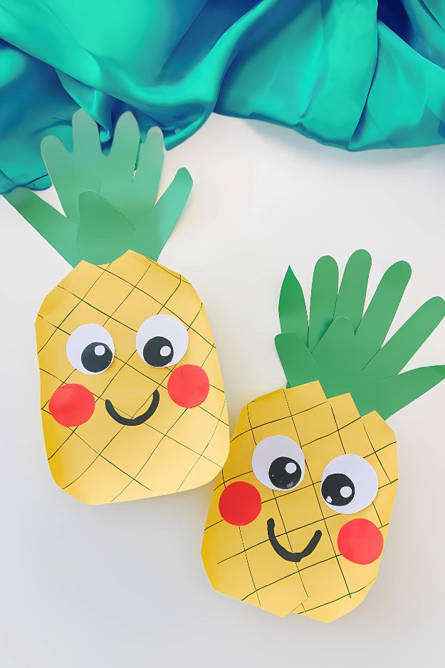 Summer crafts for kids of smiling pineapples with drawn grid patterns and handprint leaves.