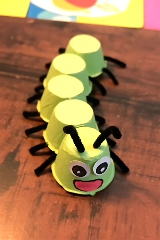Green egg carton caterpillar with googly eyes, black pipe cleaner legs, and a happy smile.