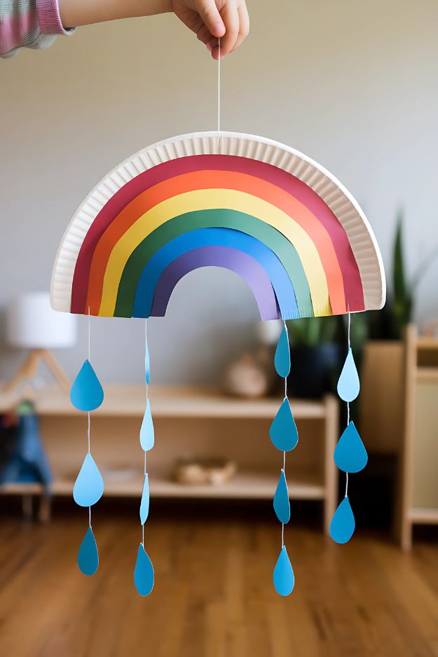 Hanging rainbow mobile made from a paper plate with colorful arches and dangling blue raindrops.