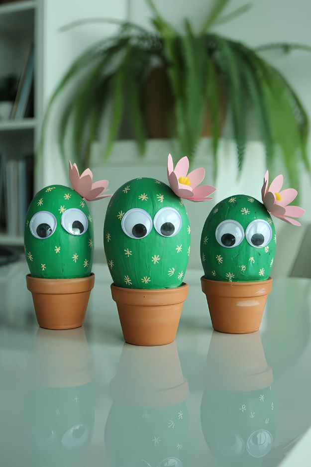 Summer crafts for kids of painted rock cacti with googly eyes and pink paper flowers in small terracotta pots.