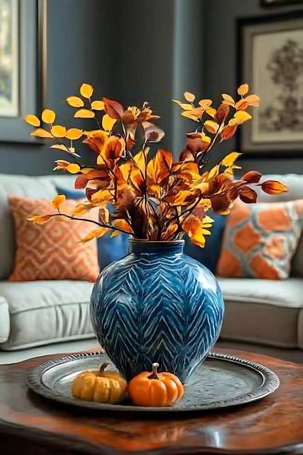 Blue vase with orange fall branches and mini pumpkins on metal tray.