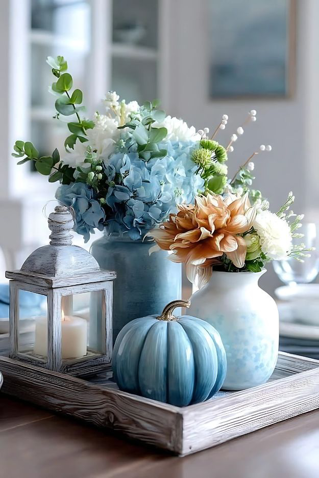 Light blue pumpkin, fall florals, and lantern in rustic tray on coffee table.