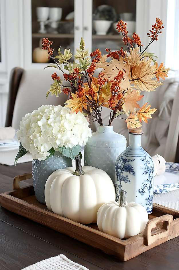 Elegant fall centerpiece with white pumpkins and blue floral vases on wooden tray