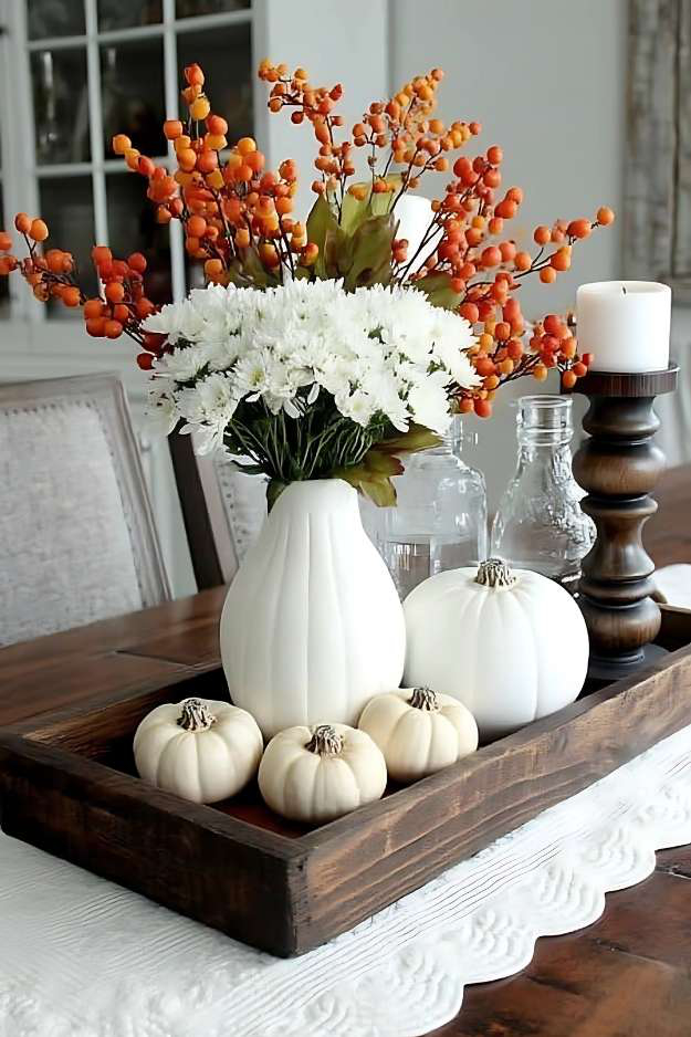White vase, pumpkins, white florals, and orange berries in a wooden tray
