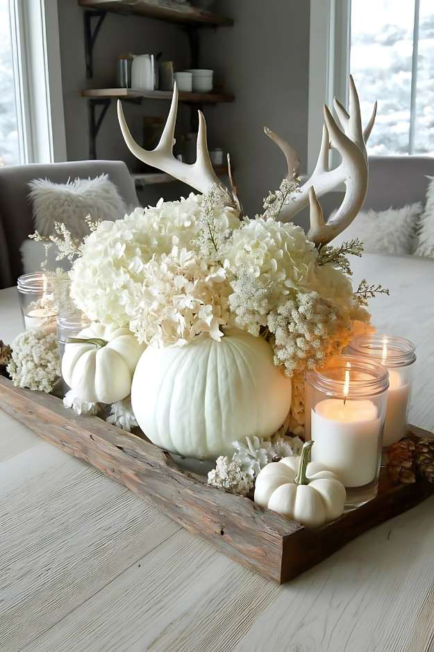 White pumpkin with antlers, soft florals, and candles on a rustic tray