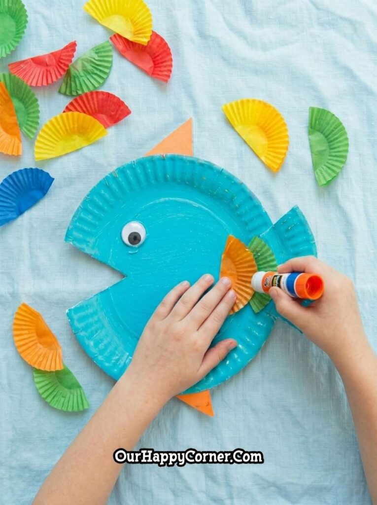 Child gluing colorful cupcake liner scales