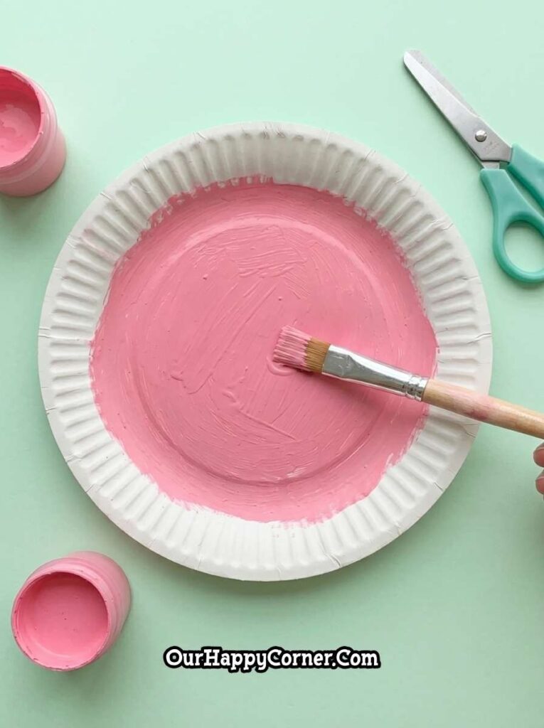 Painting paper plate pink to create watermelon base