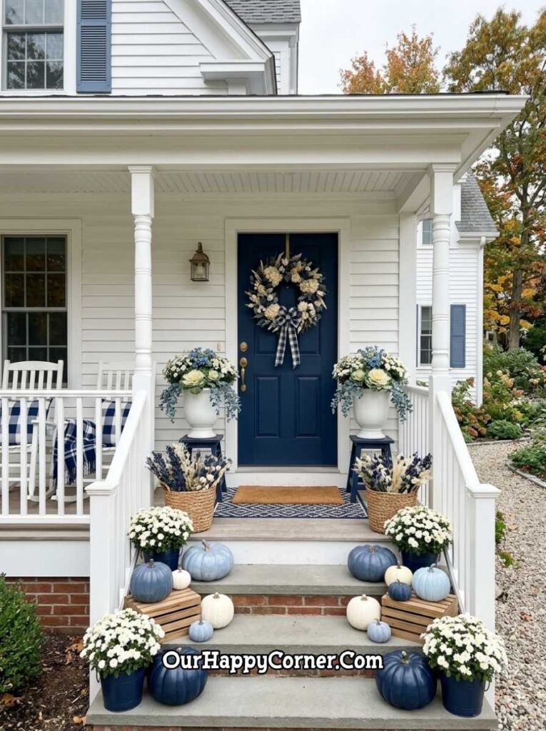 White colonial front porch with navy blue door, blue and white hydrangea wreath with plaid bow, white urns with blue floral arrangements, blue and white pumpkins on steps with white mums