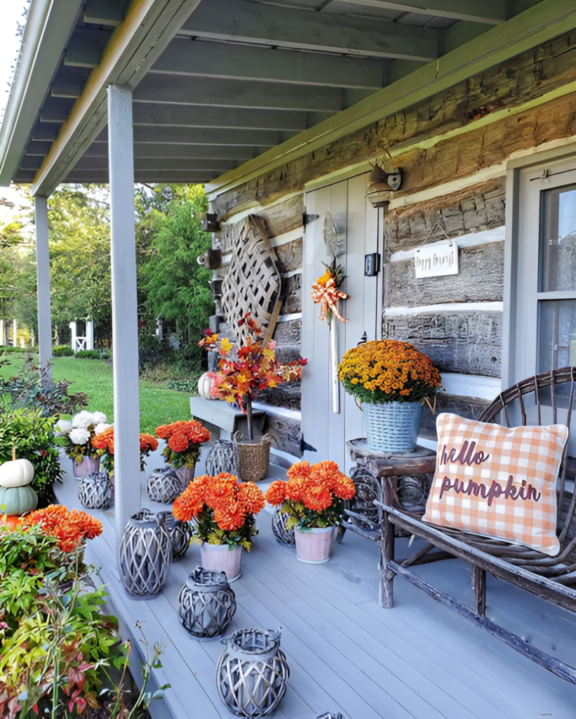 A cozy front porch decorated with vibrant orange mums, lanterns, and autumn foliage, featuring a rustic wooden bench with an orange gingham pillow that says "hello pumpkin."