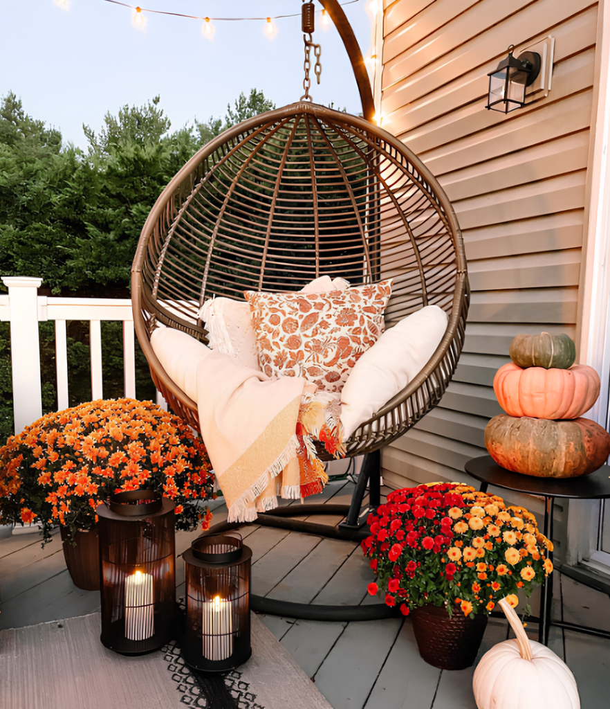 Outdoor hanging chair with autumn pillows, surrounded by pumpkins, lanterns, and string lights.