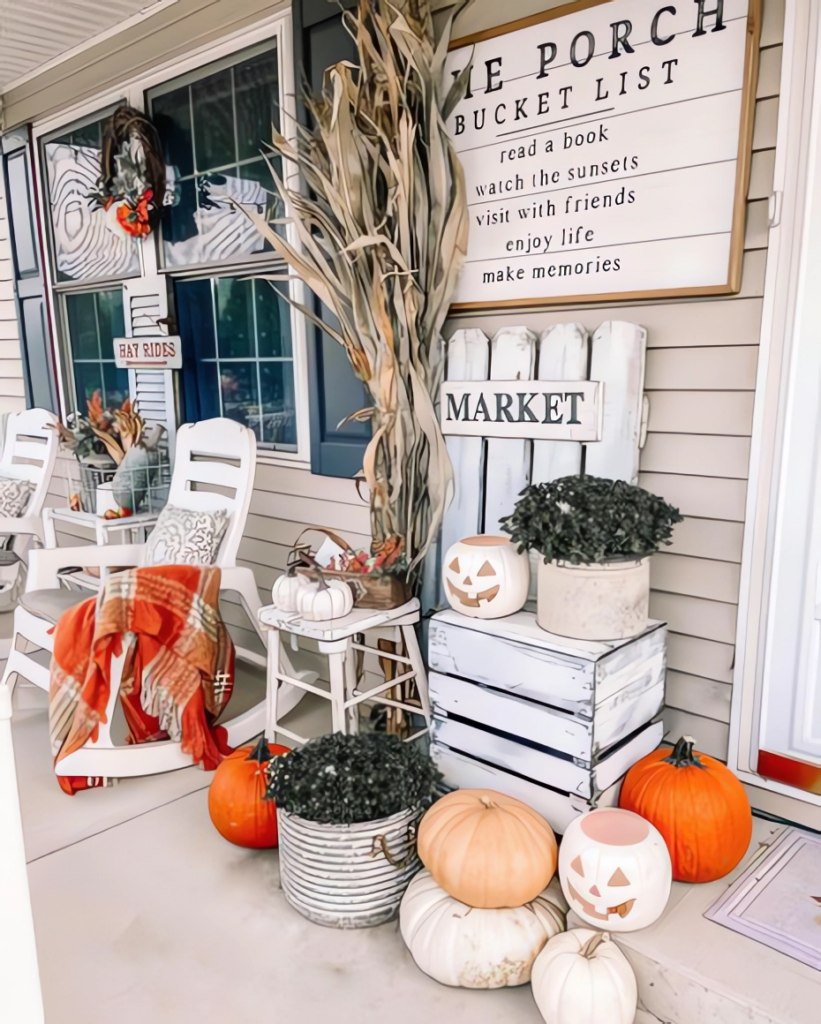 A farmhouse-style porch decorated for fall with pumpkins, plants, and signage.