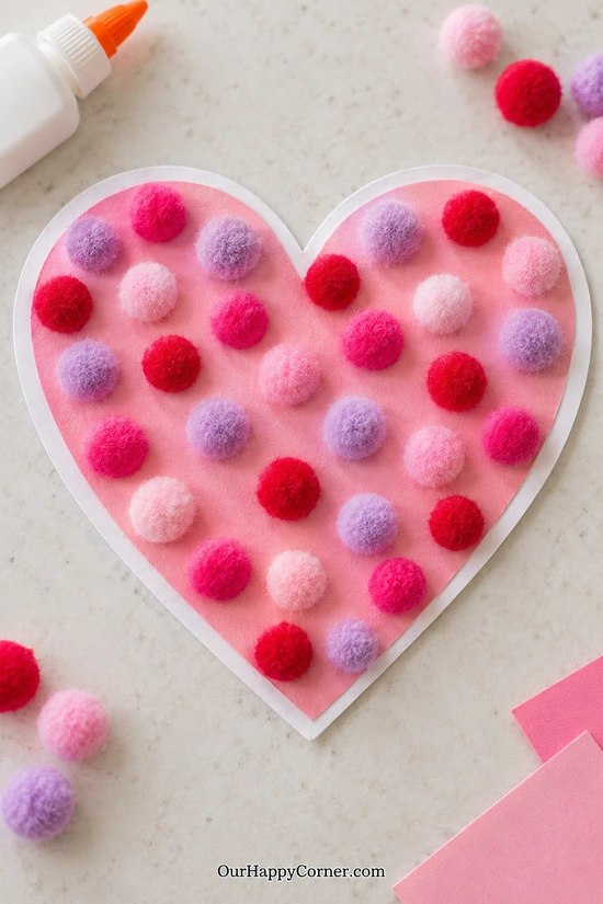 Pink paper heart collage with colorful fuzzy pom-poms