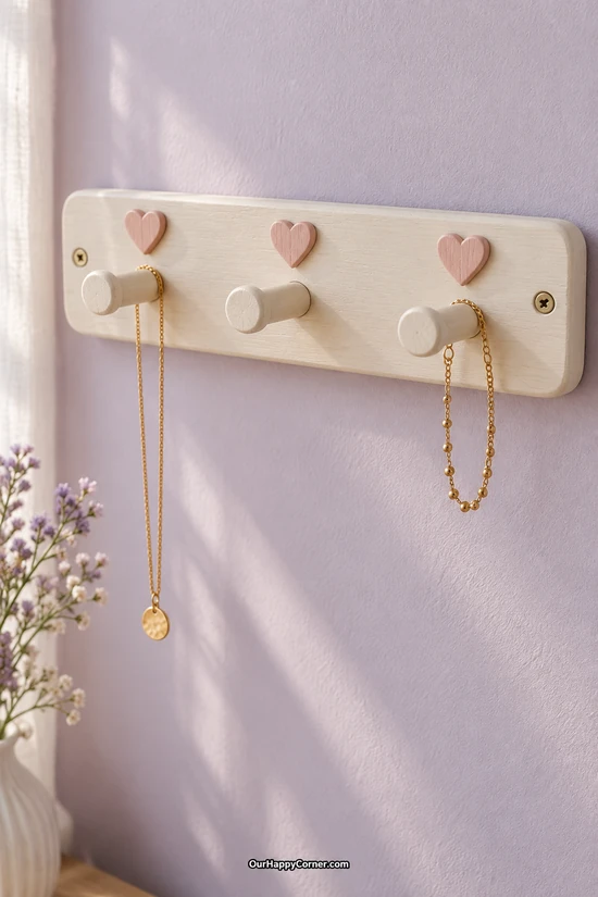 Ivory wooden wall rack with three pegs, pink hearts, and hanging gold necklaces